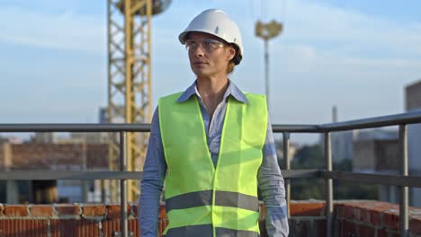 Portrait-shot-of-the-young-Caucasian-beautiful-woman-constructor-or-foreman-in-hardhat-and-goggles-standing-in-front-of-the-camera-at-the-building-site-and-looking-both-sides-while-turning-her-head.